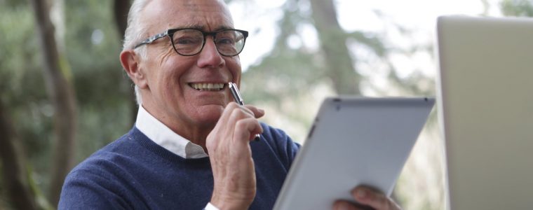 man in blue sweater holding white tablet computer